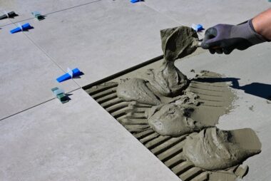 pexels-photo-11806477-11806477 Close-up of a gloved hand applying mortar for ceramic tile installation outdoors.