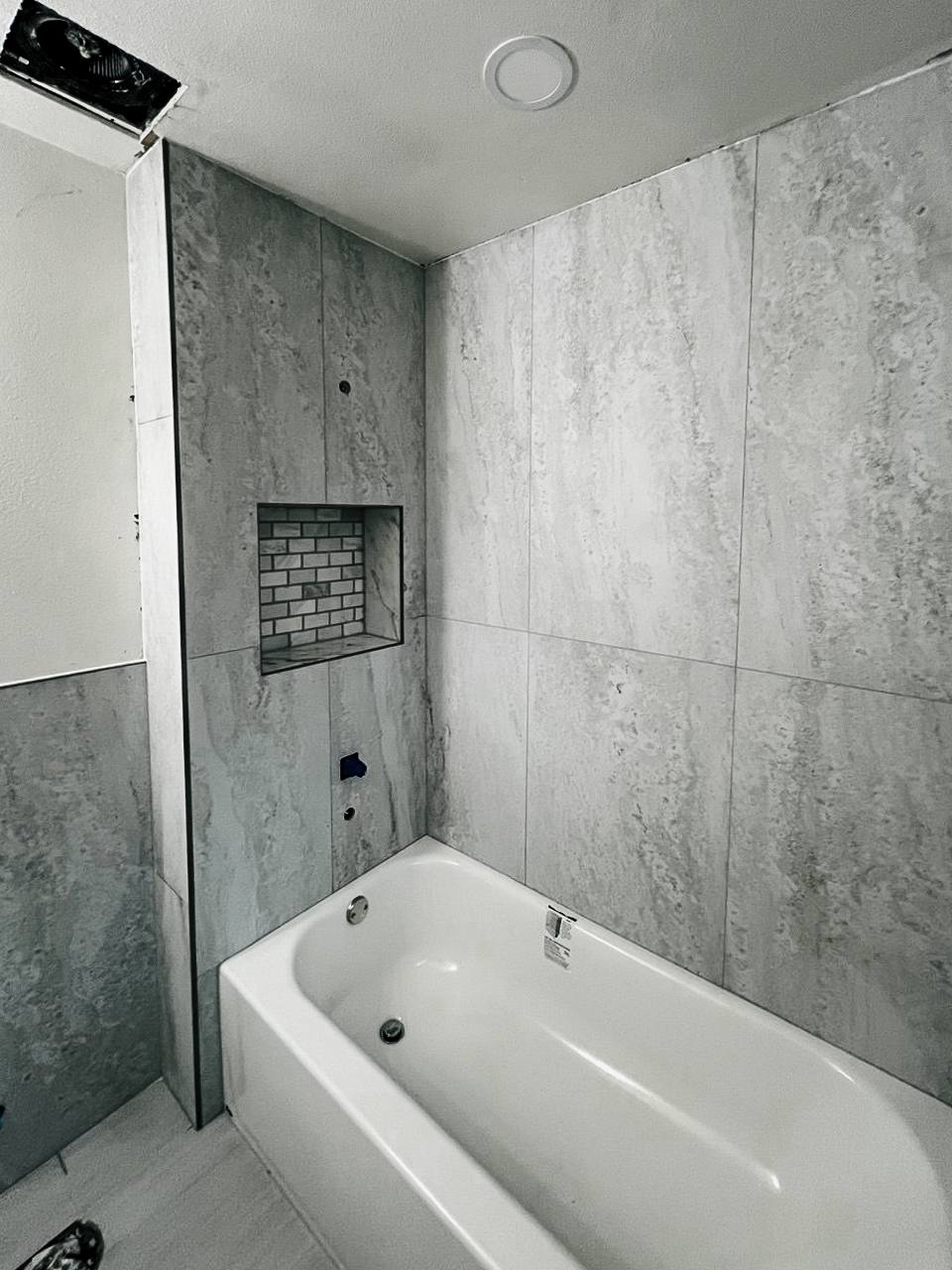 Modern bathroom tub surround with large gray stone-look tiles and a built-in niche featuring a subway mosaic accent by professional tiler.