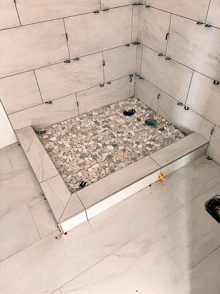 photo_19_2025-03-01_20-04-21 Tiler made modern walk-in bathroom shower under construction with large-format tiles and a pebble mosaic floor.