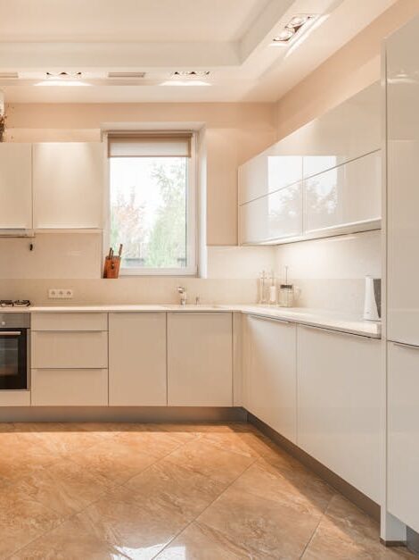 Stylish interior of kitchen with white cupboards and built in oven and stove under lamps on ceiling