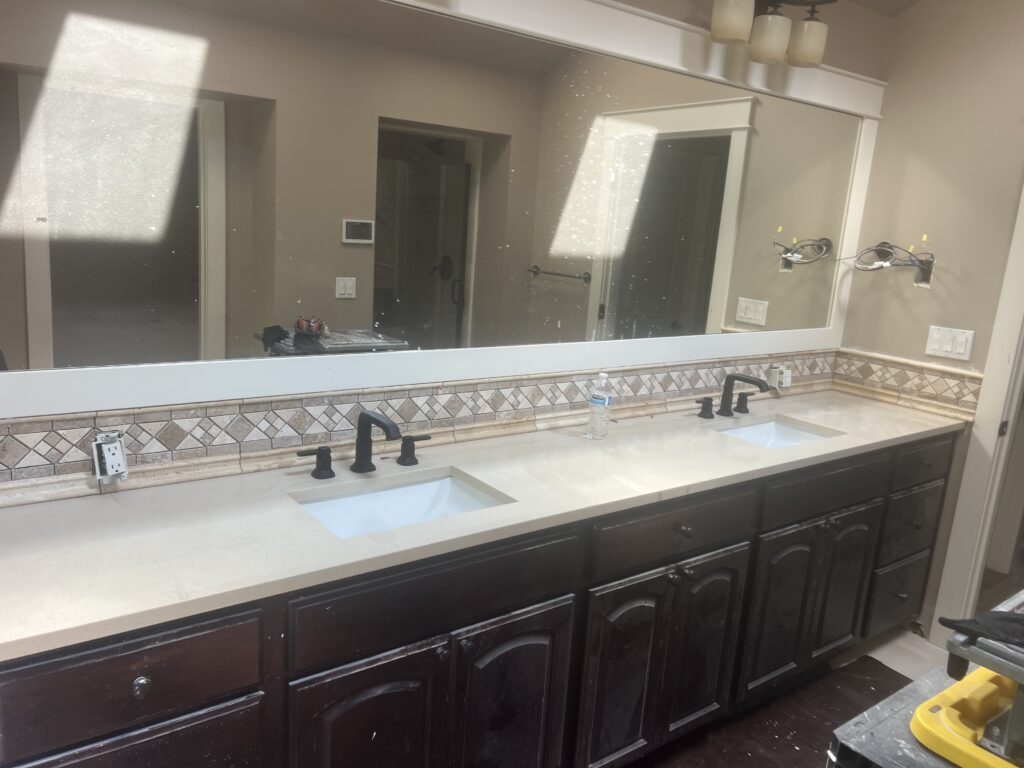 Finished bathroom with a double vanity, wide mirror, and tile detail above the counter