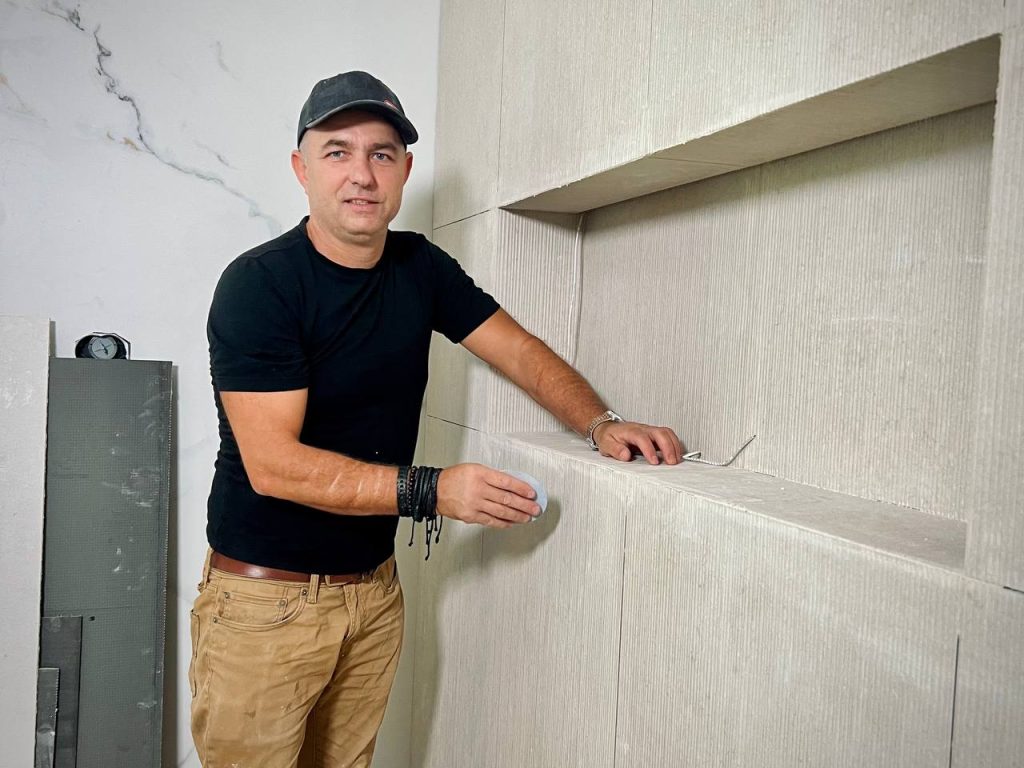 Andzhei standing beside a finished tiled shower with a niche
