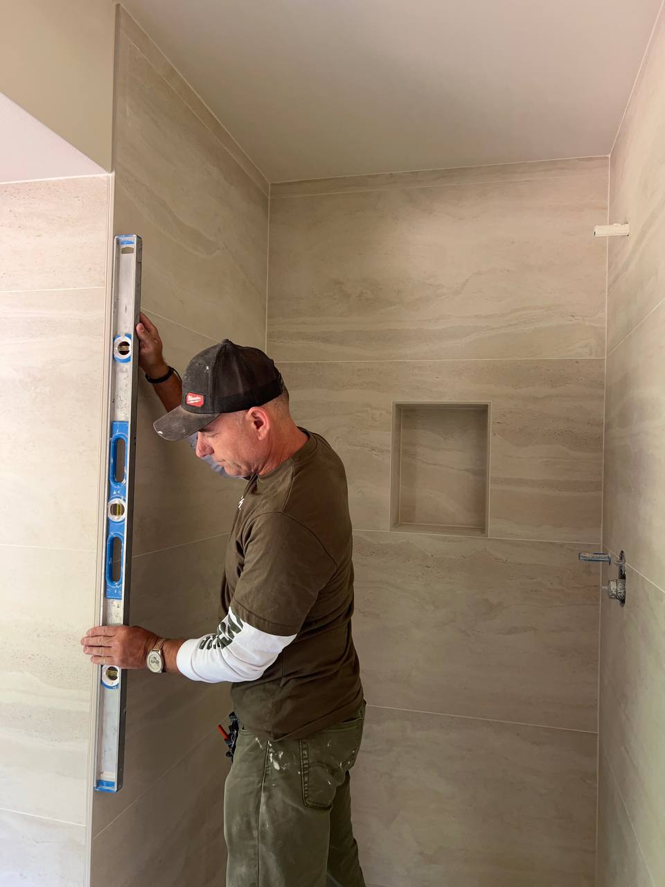 Andzhei checking a large-format tiled shower wall with a level — Ability Tiles, Greater Seattle