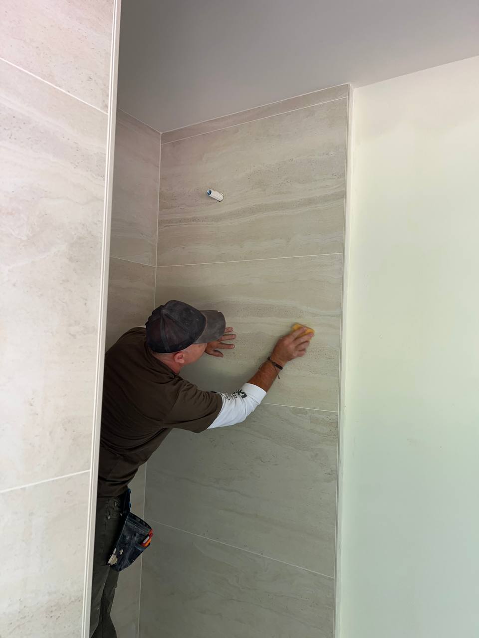 Andzhei cleaning large-format shower wall tile after installation